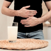 Man holding stomach in pain from a glass of milk in front of him
