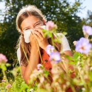girl with hay fever holding tissue around flowers